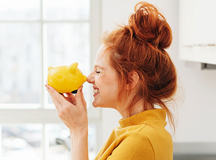 eine Frau, die ein gelbes Sparschwein mit der Nase anstupst