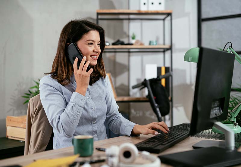 Junge Frau im Büro sitzt vor dem PC und telefoniert.