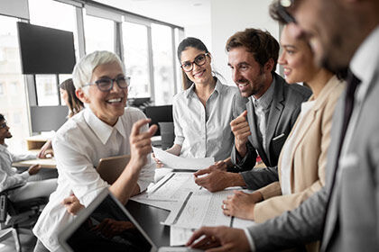 eine Gruppe von Menschen, die um einen Tisch sitzen und zwei Männer die Hände schütteln