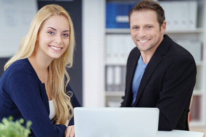 zwei Personen sitzen an einem Tisch mit einem Laptop und lächeln